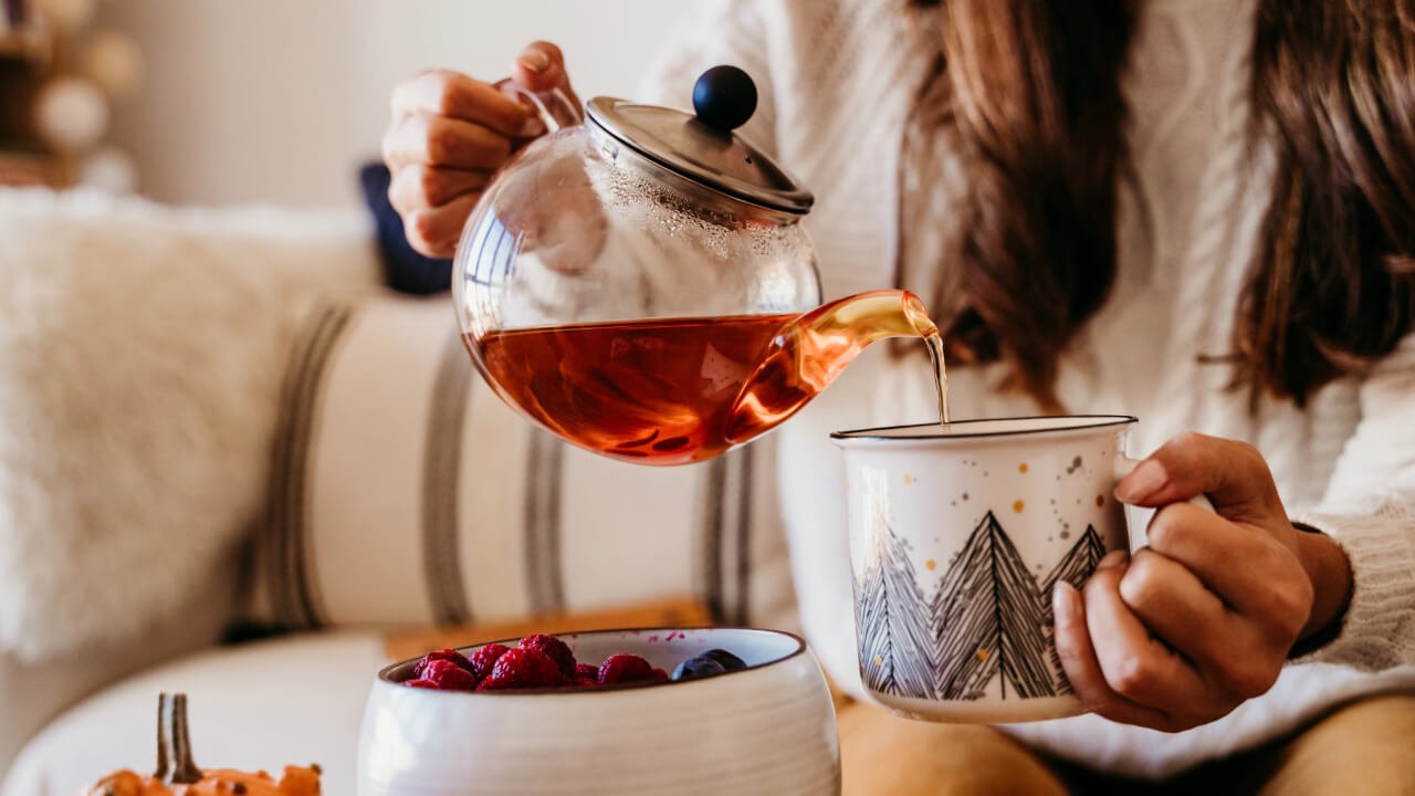 Persona sirviendo té caliente en una taza decorativa, capturando la calidez y la tradición del té colombiano en un ambiente acogedor.